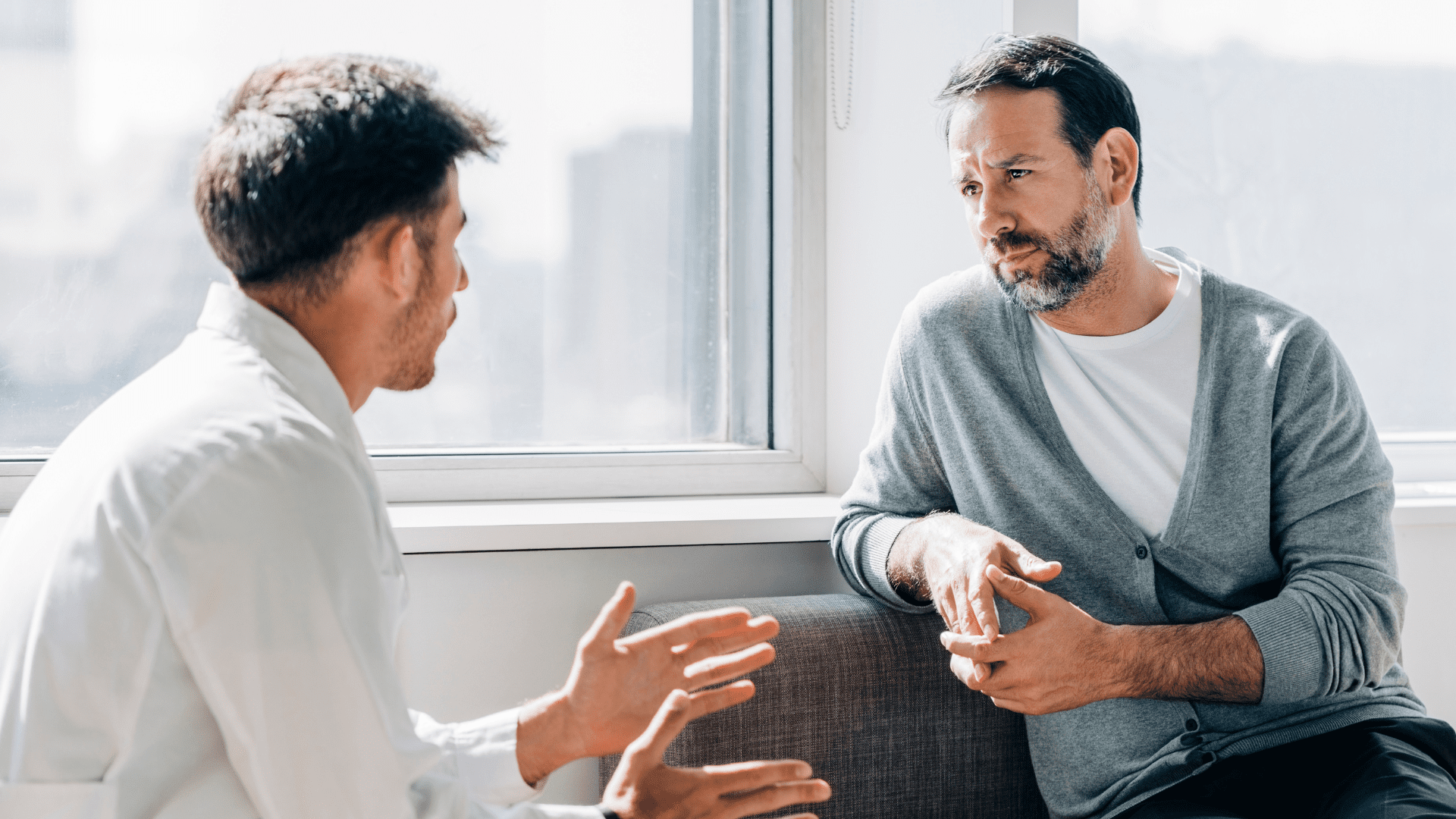 Dos personas conversan en una sesión, junto a una ventana